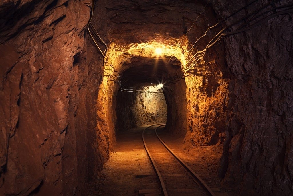 Dimly lit underground mine tunnel with rough, rocky walls. As a professional tours specialist