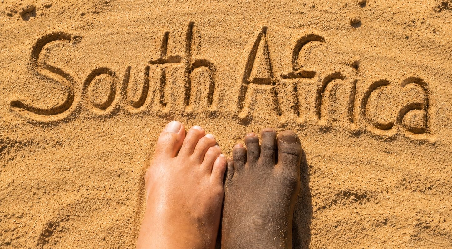 Two bare feet—one lighter-skinned, one darker-skinned—stand side by side on sand