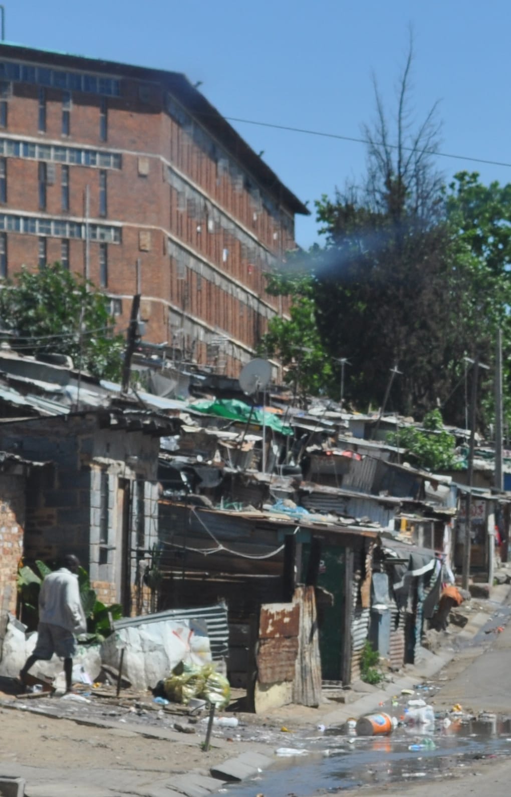 A man walks near makeshift homes of metal sheets and bricks, piles of bags