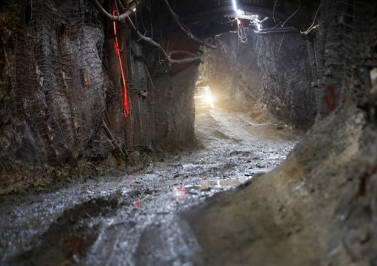 A muddy, dimly lit tunnel inside a mine with rough rocky walls, metal supports