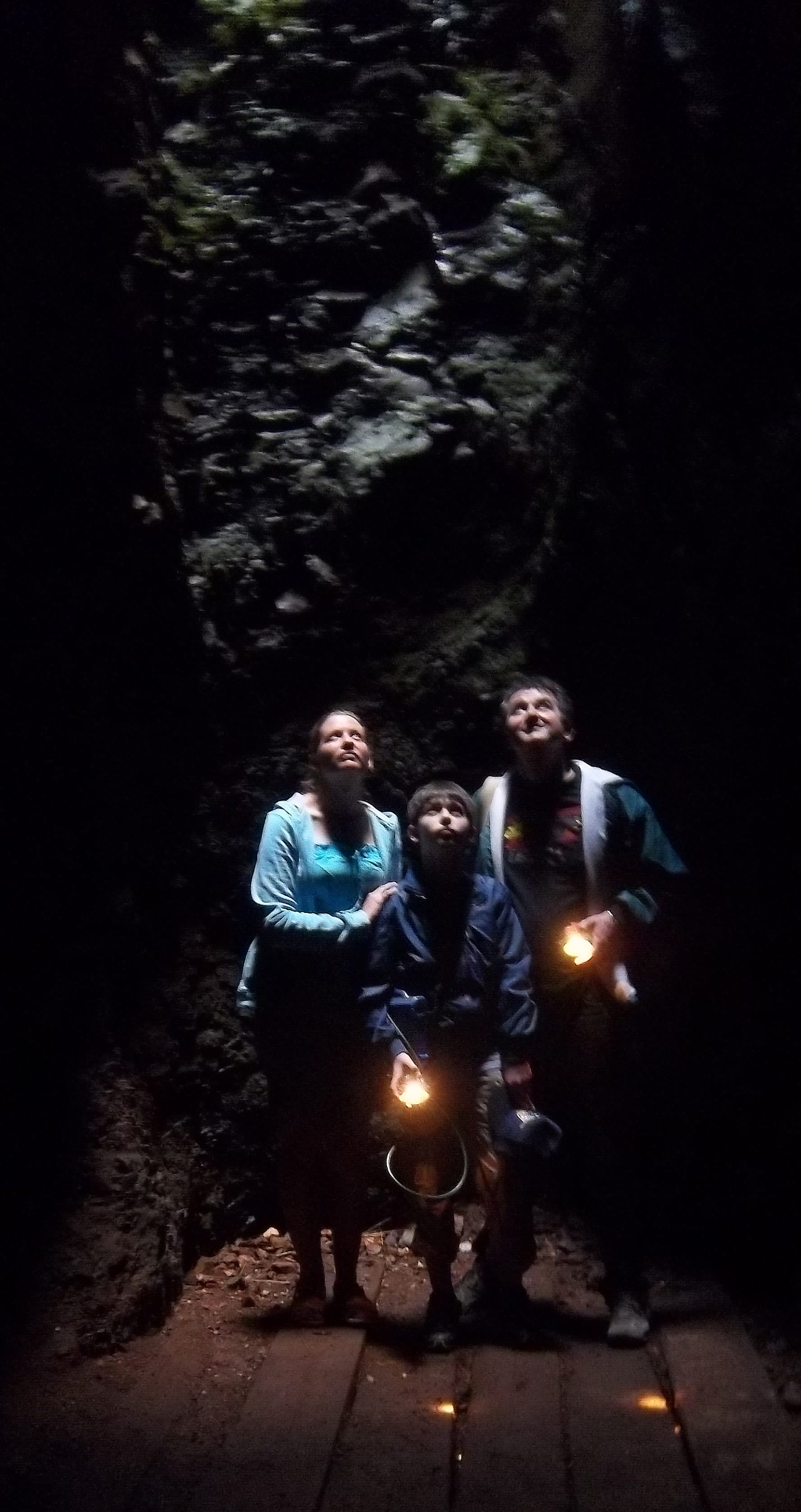 Three people stand in a dark cave, illuminated by small handheld torches