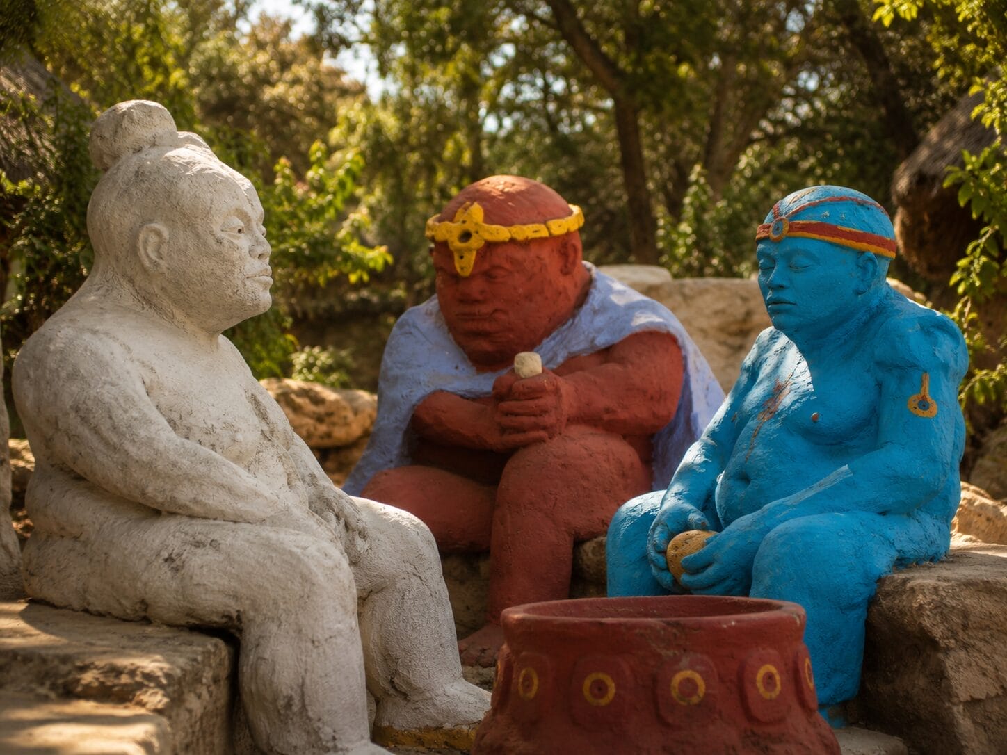 Three colourful stone statues sit around a circular red structure outdoors